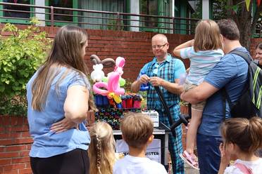 Jahresfest 2025 – Eine Personengruppe schaut einem Ballonkünstler zu. 